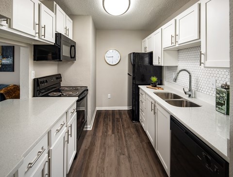 A kitchen with white cabinets and a black fridge.