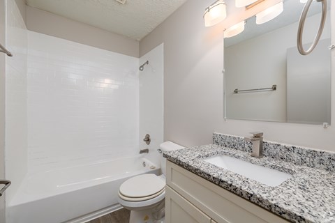 A white bathroom with a granite counter top and a white toilet.
