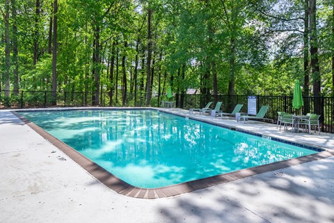 A swimming pool surrounded by trees and chairs.