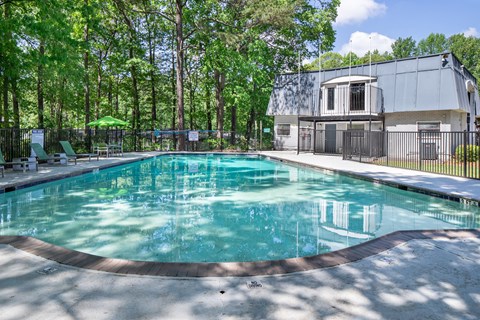 A swimming pool surrounded by trees and a building in the background.