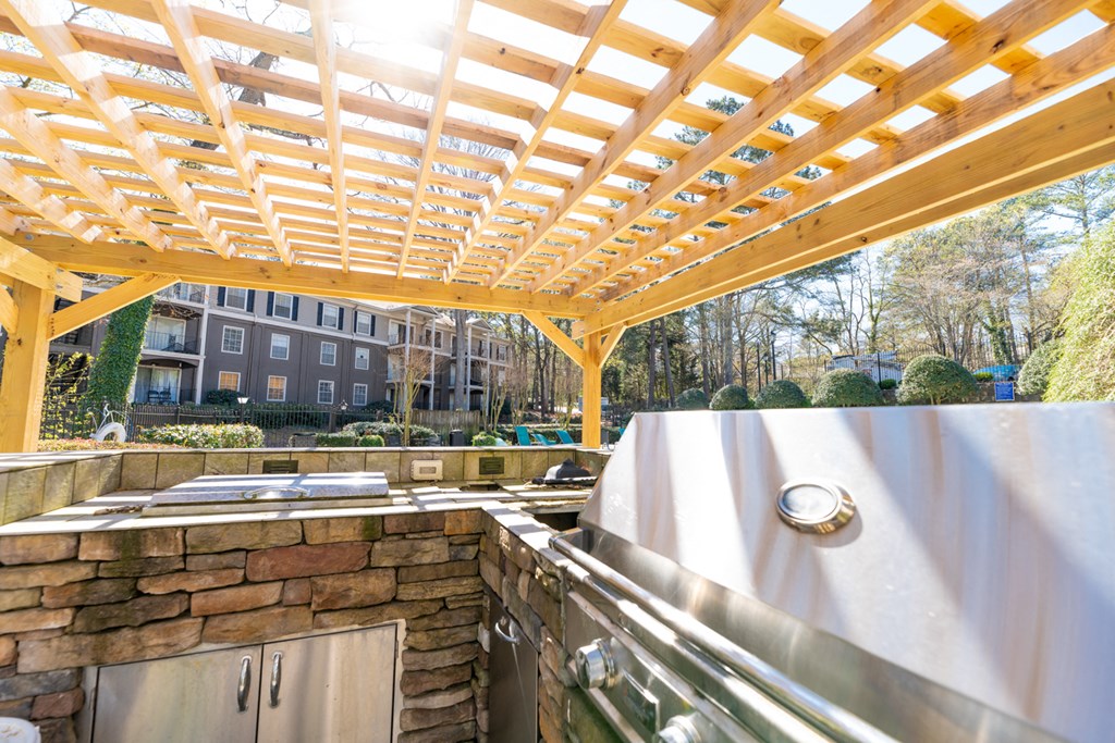 the outdoor kitchen is under a wooden roof and has a stone wall and a counter