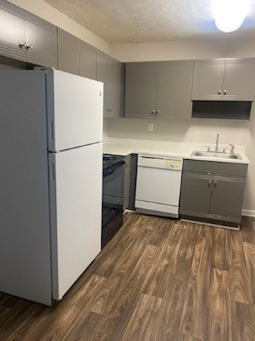 A white refrigerator is in a kitchen with wood flooring.