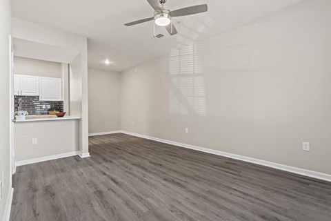 an empty living room with a ceiling fan and a kitchen