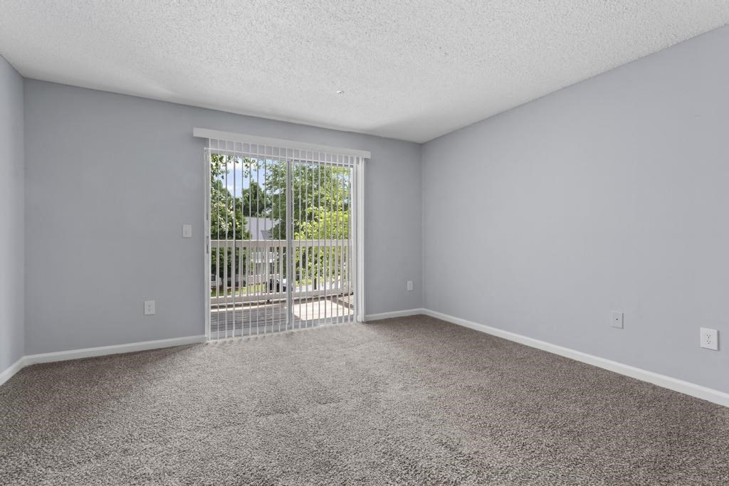 an empty living room with a sliding glass door to a balcony