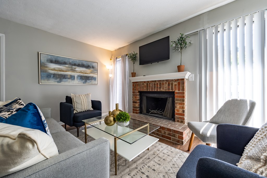 A living room with a grey couch, a blue chair, a glass coffee table, a fireplace, and a painting on the wall.