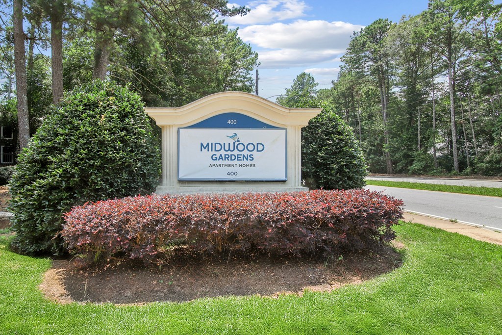 A sign for Midwood Gardens is surrounded by shrubbery.