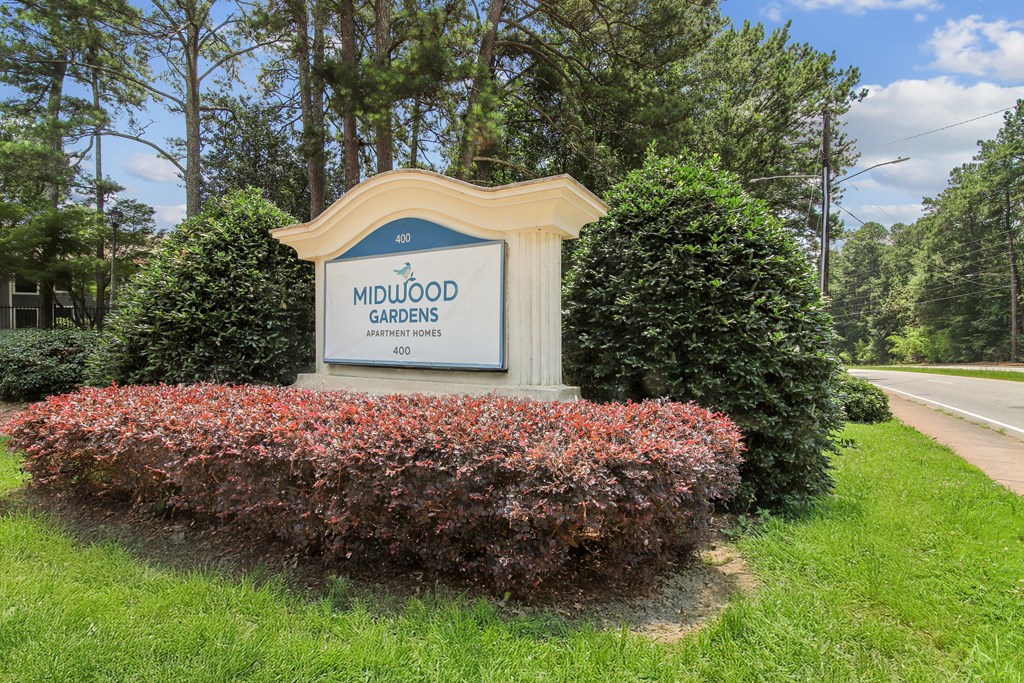 A sign for Midwood Gardens is surrounded by shrubbery.