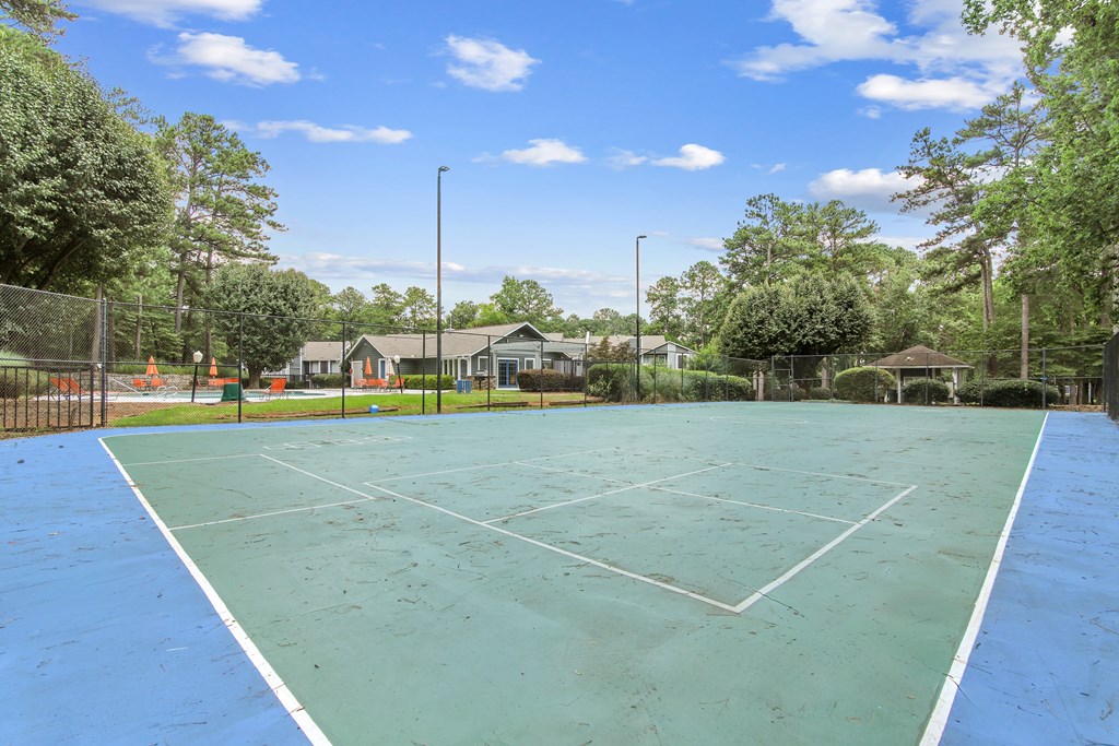 A tennis court surrounded by trees and a fence.