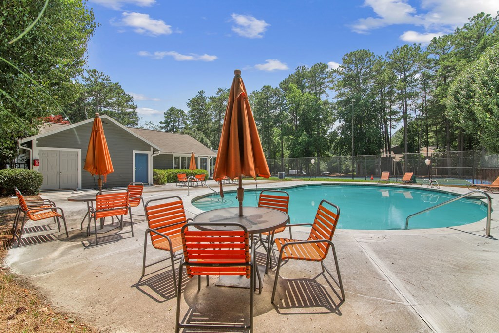 A poolside table with chairs and umbrellas is set up next to a swimming pool.