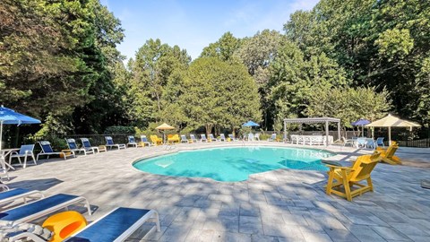 the pool is surrounded by chairs and umbrellas and trees