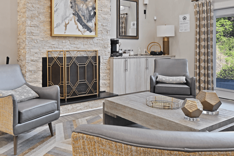 A living room with a grey chair, a grey ottoman, a coffee table, a fireplace, and a painting on the wall.