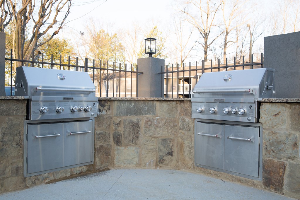 two stainless steel gas barbecue grills on a stone wall