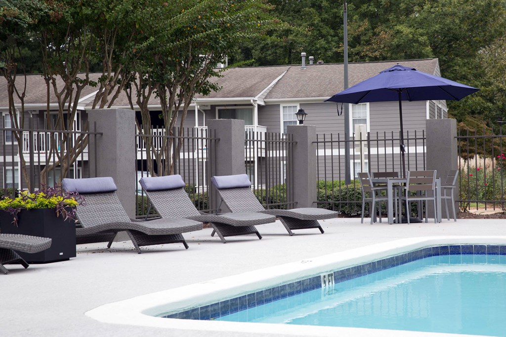 a swimming pool with chaise lounge chairs and an umbrella in front of a house