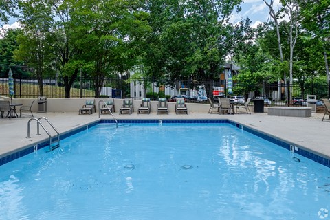 A large blue swimming pool surrounded by trees and lounge chairs.