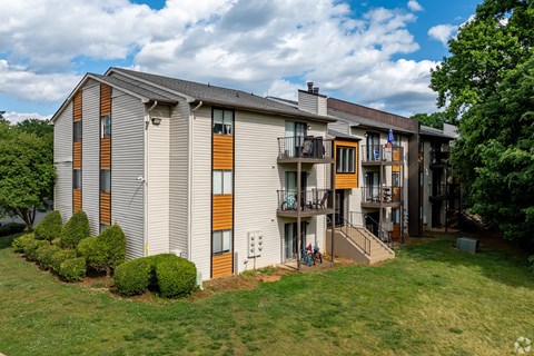 A modern apartment building with a balcony and a small garden in front.
