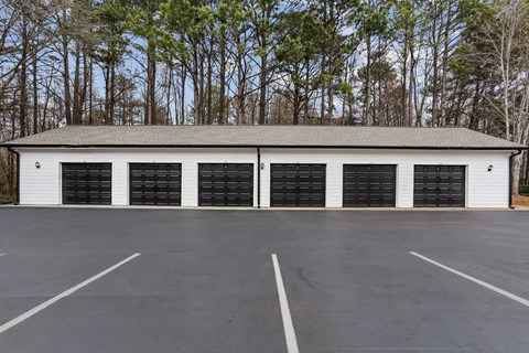 A large white building with black garage doors in the middle of a parking lot.