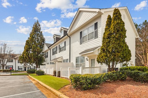 A white two-story house with a grey roof and a white fence.