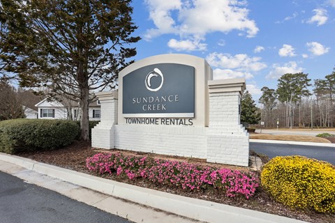 A sign for Sundance Creek Townhome Rentals is surrounded by flowers and greenery.