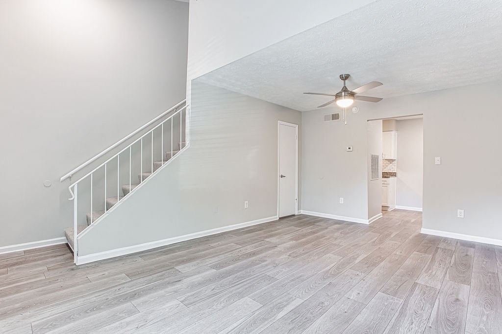 an empty living room with a ceiling fan and a staircase