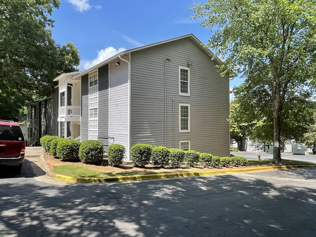 a grey apartment building with a parking lot and some bushes