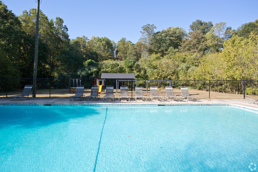 A swimming pool surrounded by trees and chairs.