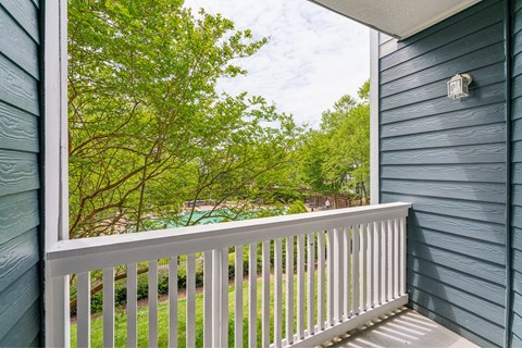A balcony with a view of a green lawn and trees.