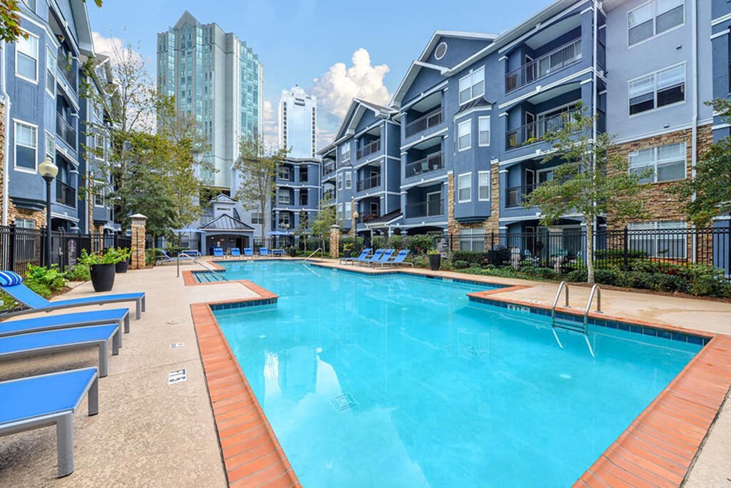 A swimming pool surrounded by blue lounge chairs and apartment buildings.