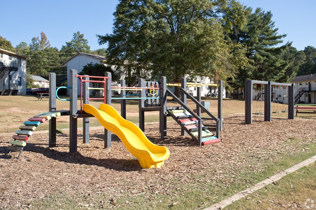 A playground with a yellow slide and a red and grey climbing frame.