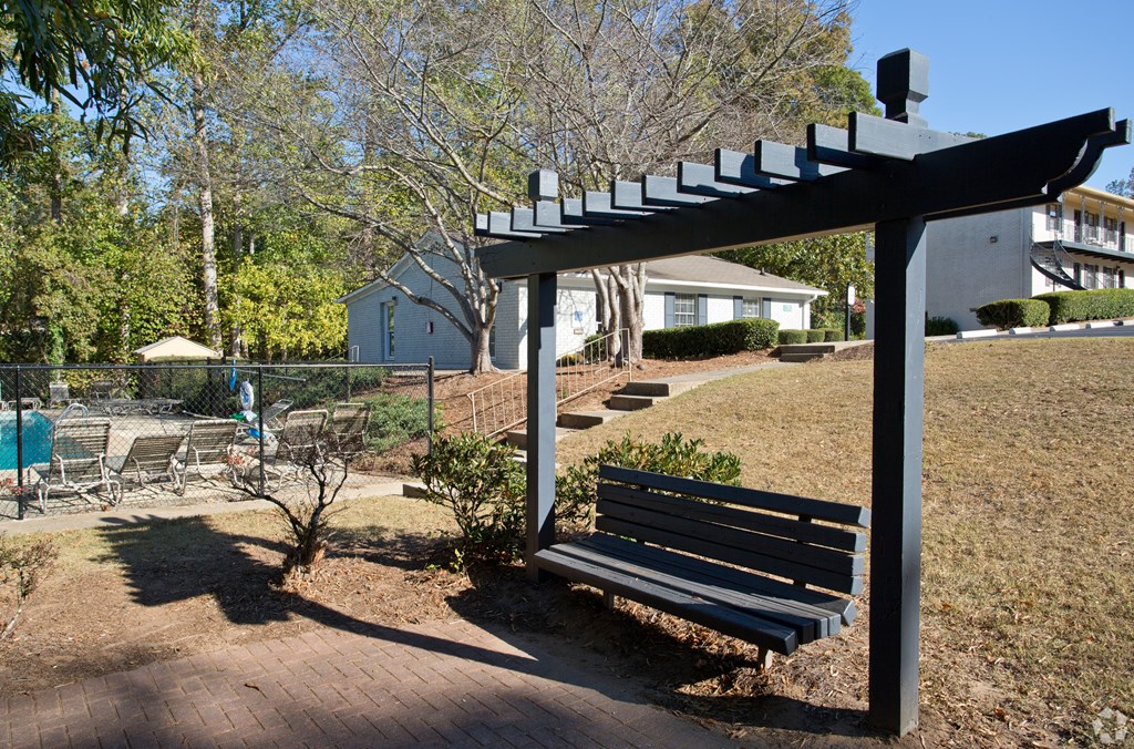 A park bench under a black metal pergola.