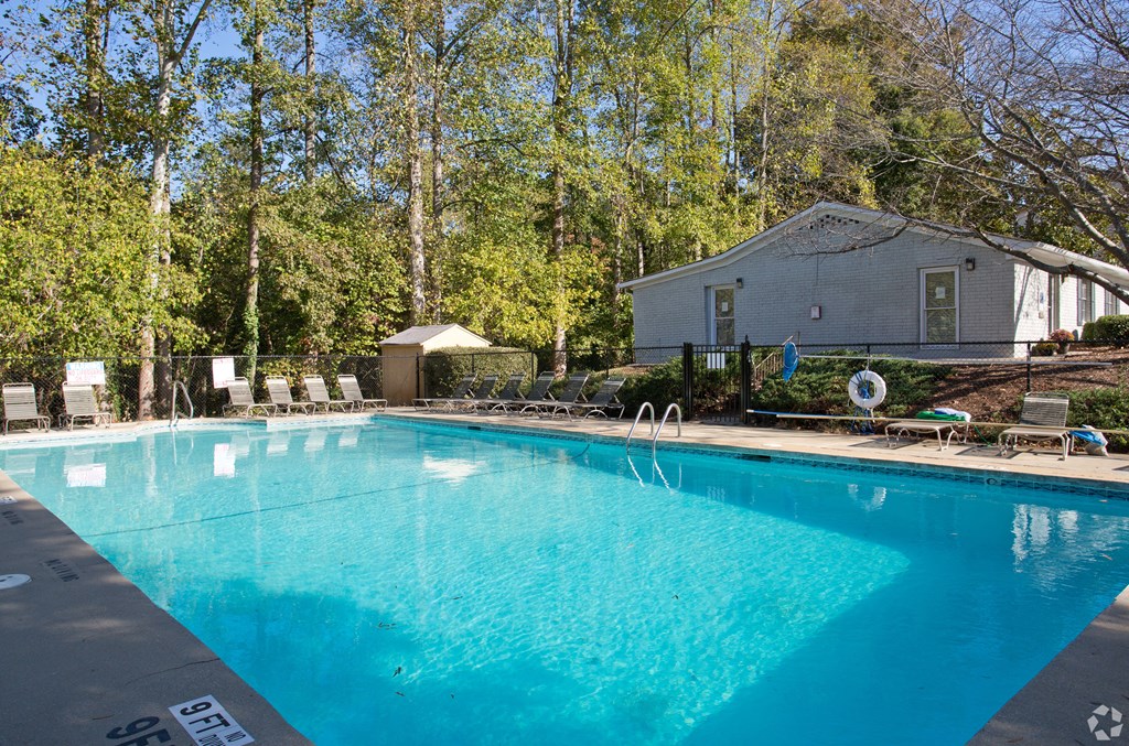 A swimming pool surrounded by trees and a house in the background.