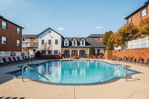 A swimming pool surrounded by lounge chairs and buildings in the background.