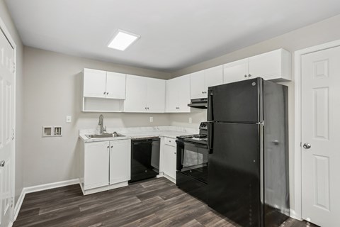 A black refrigerator is in a kitchen with white cabinets.