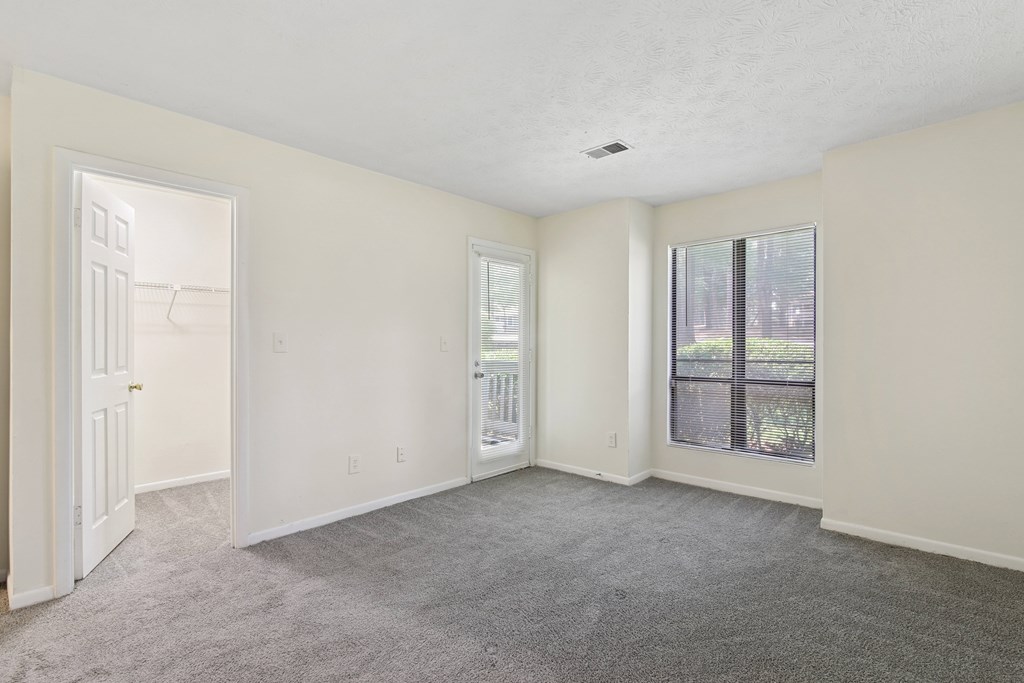 A room with a grey carpet and a window overlooking a balcony.
