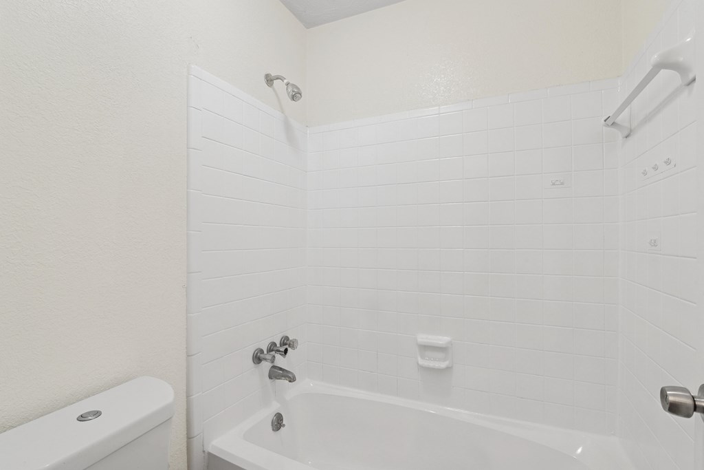 A white bathroom with a toilet, tub, and towel rack.