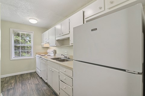 A white refrigerator in a kitchen with wooden floors and white cabinets.