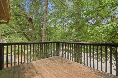 A balcony with a black railing and wooden floor overlooks a lush green forest.