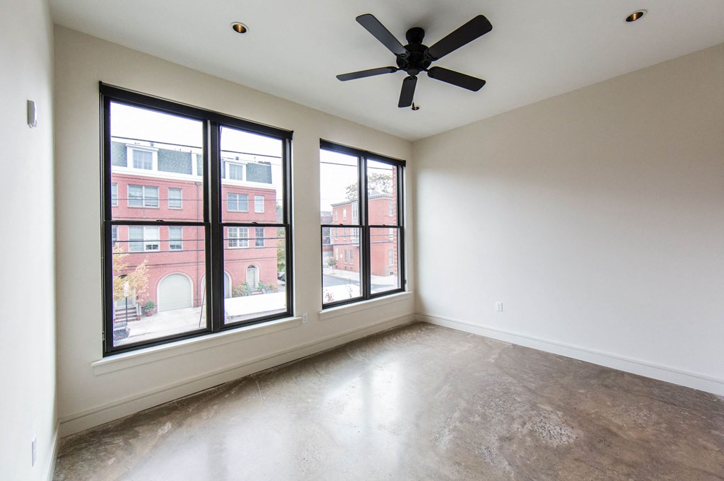 an empty living room with large windows and a ceiling fan