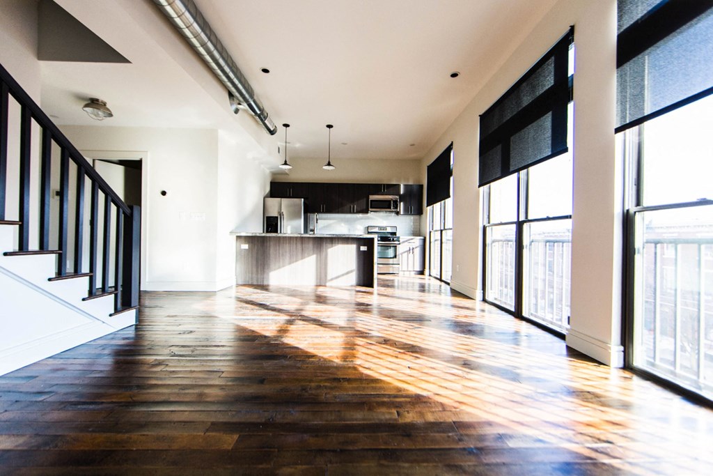 an empty living room and kitchen with windows and wood floors