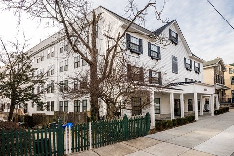 A white two-story building with a green fence in front.