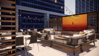A modern outdoor seating area with a large screen displaying a sunset.