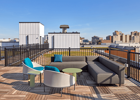 a rooftop deck with a couch and tables and a city in the background