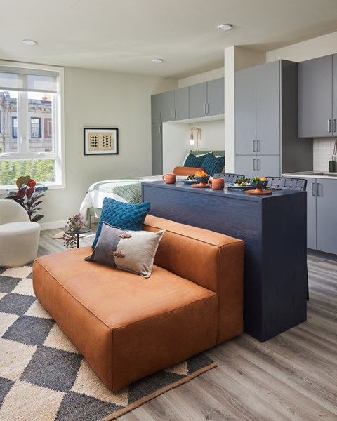 A snapshot of a LVL West studio apartment floorplan with a bed by a large window,  a kitchen, bar seating dining area, and a couch and armchair.