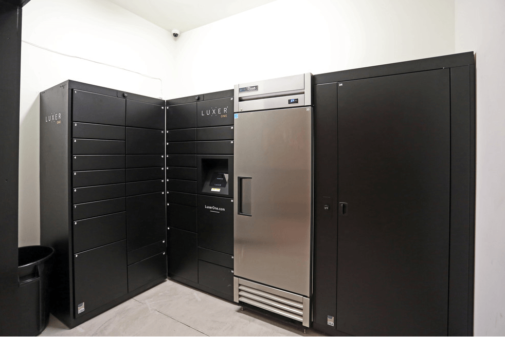 a row of black lockers in a white room with a stainless steel refrigerator
