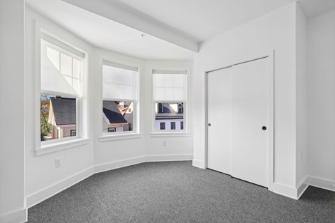 A white room with a grey carpet and three windows.