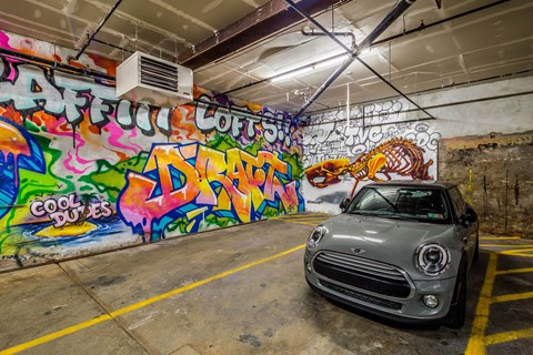 A grey Mini Cooper is parked in a garage with graffiti on the walls.
