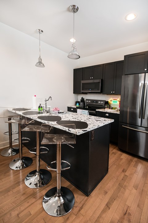 A kitchen with black cabinets and a marble island.
