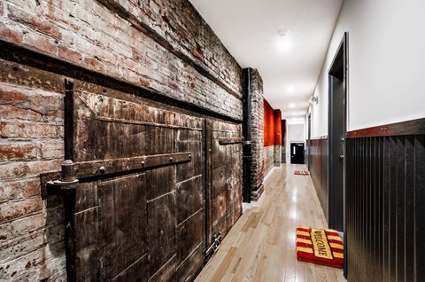 A long hallway with a brick wall on the left and a wooden floor.