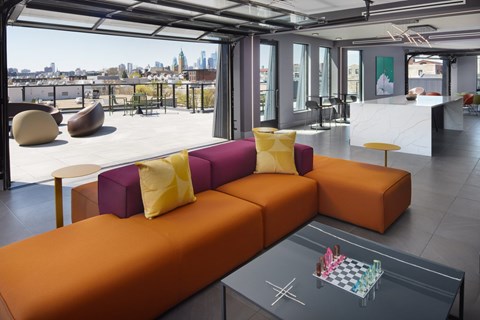 A modern living room with a large orange sofa and a glass table with a chess board on it.