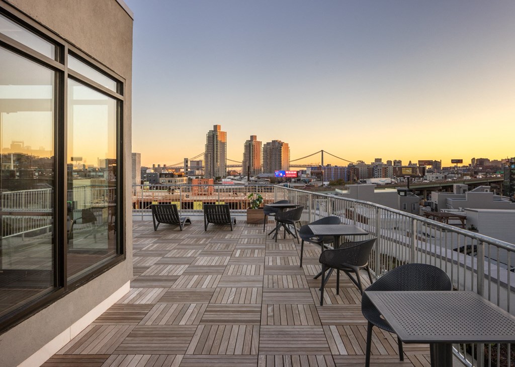 a balcony with tables and chairs overlooking a city at sunset