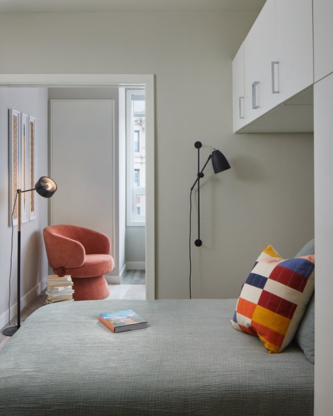 A snapshot of the bedroom area in LVL West 1-Bedroom floorplan. Camera is looking out from the bedroom into the living room, where the reading nook with armchair are visible.